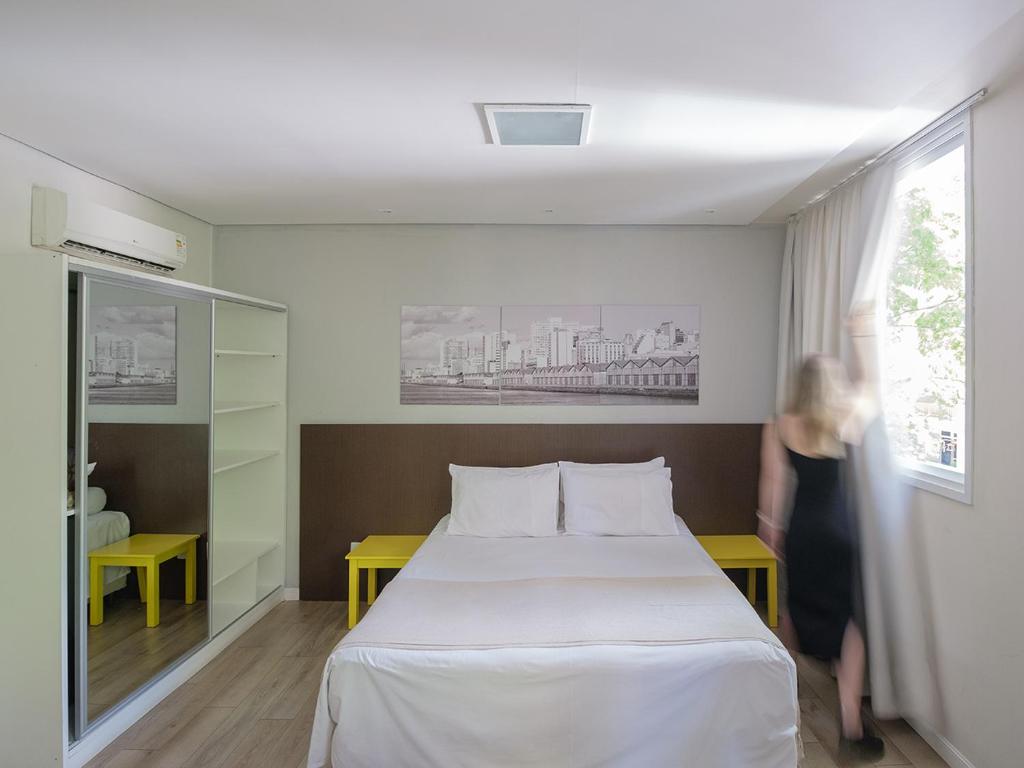 una mujer de pie junto a una cama en una habitación en Açores Flat Design- Ao lado da Casa De Cultura Mário Quintana en Porto Alegre