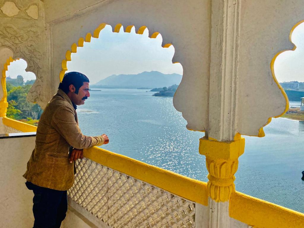 a man standing on a balcony looking at the water at Haveli BALAVH with lake facing balcony in Udaipur