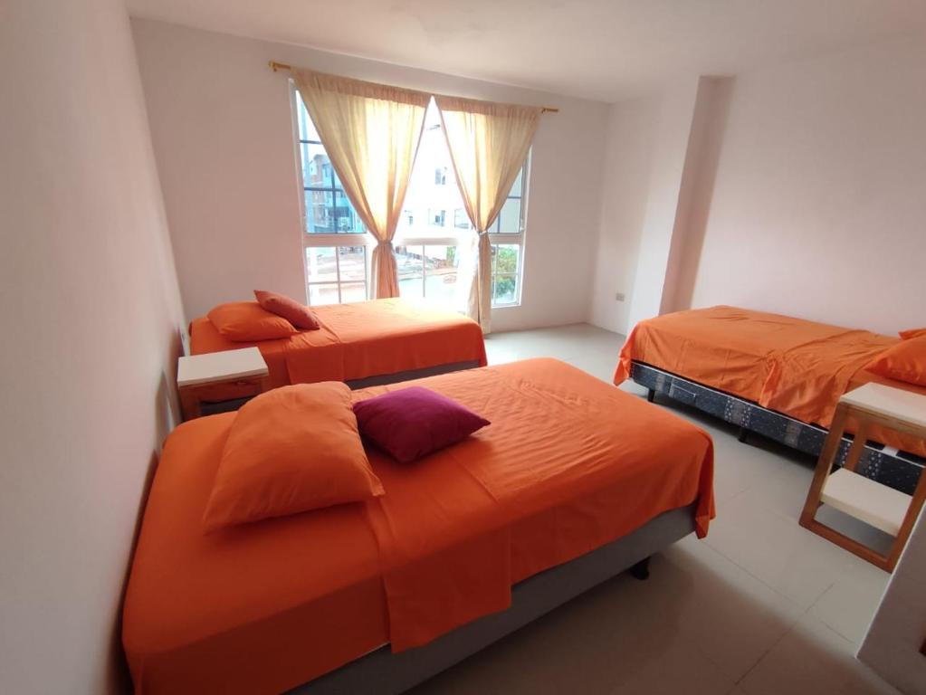 Habitación con 3 camas con sábanas de color naranja y ventana en PELICAN TOURS, en Puerto Baquerizo Moreno