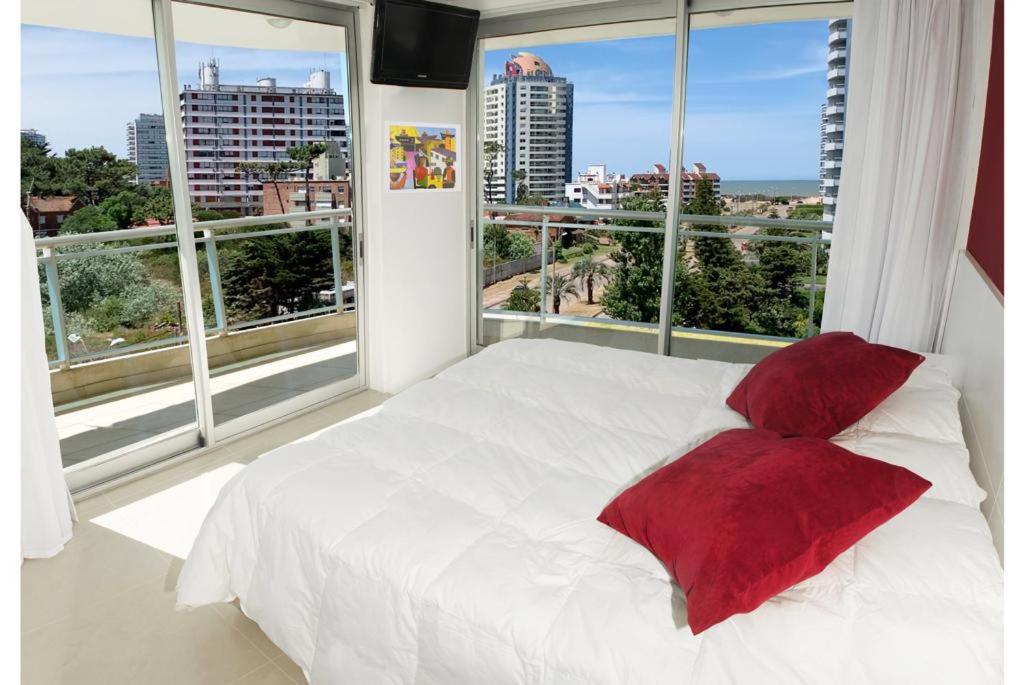 Cama blanca con almohadas rojas frente a una ventana en Sol y Luna Home&Spa, en Punta del Este