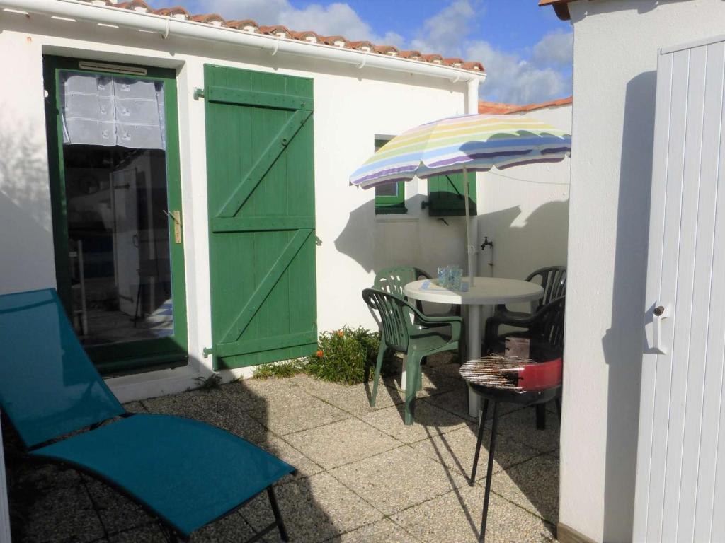 une terrasse avec une porte verte et une table avec un parasol dans l'établissement Charmante Maison avec Piscine Chauffée et Tennis, Proche Plage, Bretignolles-sur-Mer - FR-1-224A-59, à Bretignolles-sur-Mer