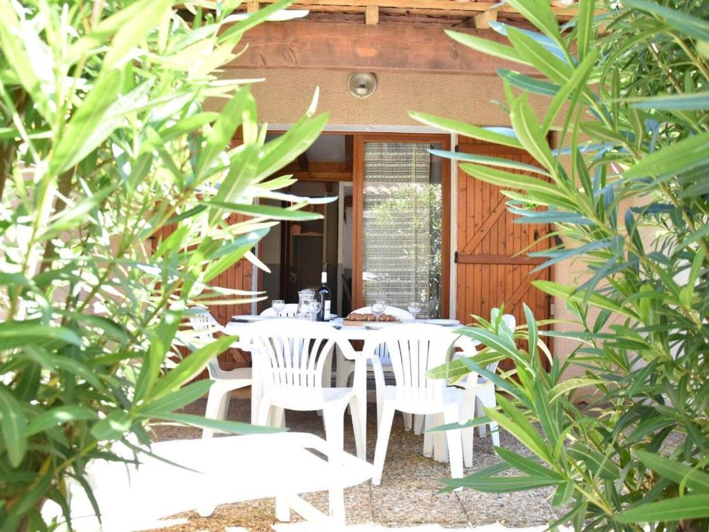 un patio avec des tables blanches, des chaises et des arbres dans l'établissement Charmant pavillon 6 couchages à 100m de la plage avec terrasse - Gruissan - FR-1-229-823, à Gruissan