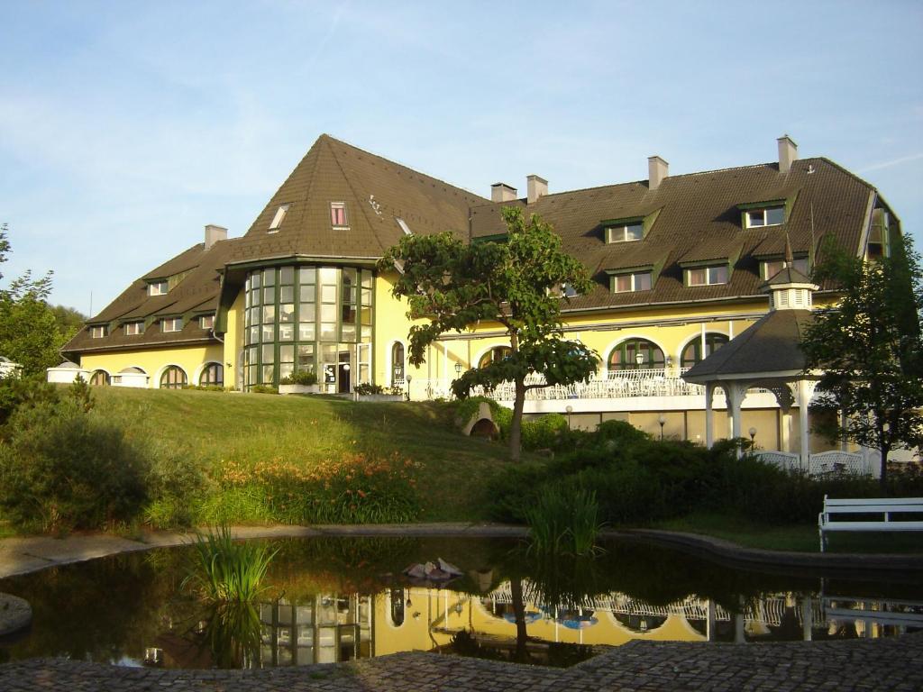 a large yellow building with a reflection in a pond at Hotel Familia in Zamárdi