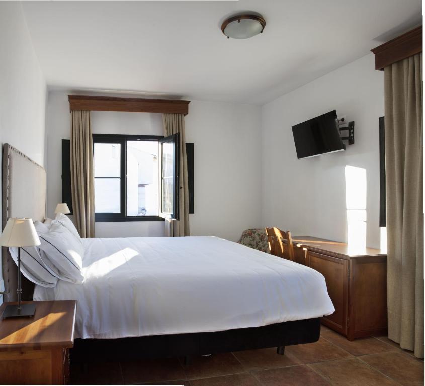 a bedroom with a white bed and a desk and a window at Hotel Tugasa Sierra y Cal in Olvera
