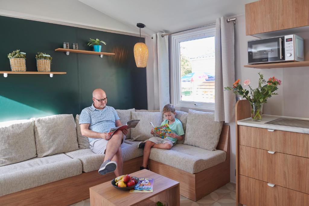 un hombre y un niño sentados en un sofá en una sala de estar en Siblu Camping Meerwijck, en Kropswolde