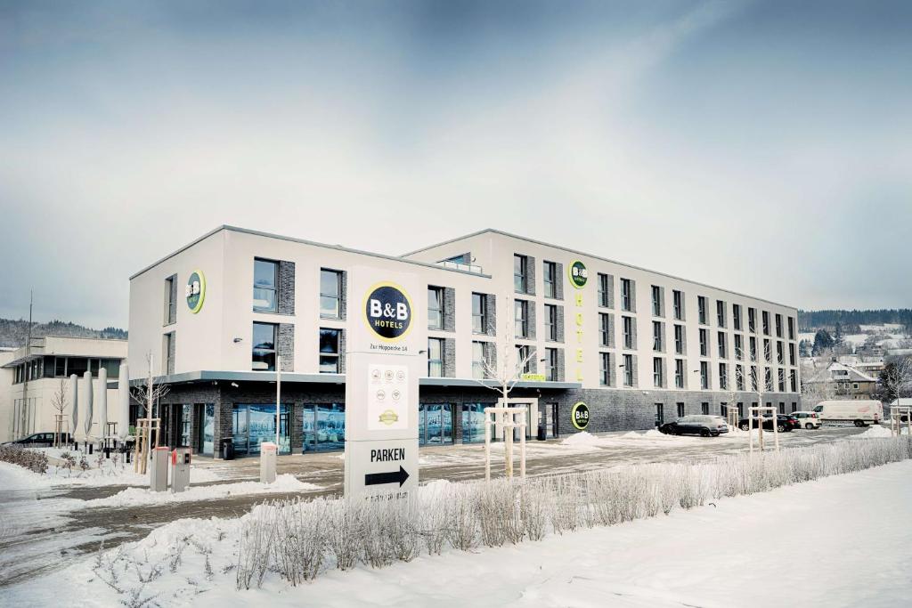 Un grand bâtiment blanc avec un panneau dans la neige dans l'établissement B&B Hotel Willingen, à Willingen