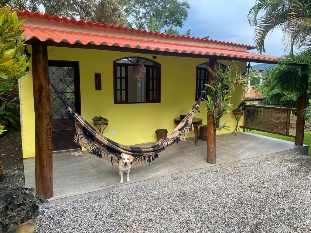 un perro parado frente a una casa con una hamaca en Vale da Paz en Guapimirim