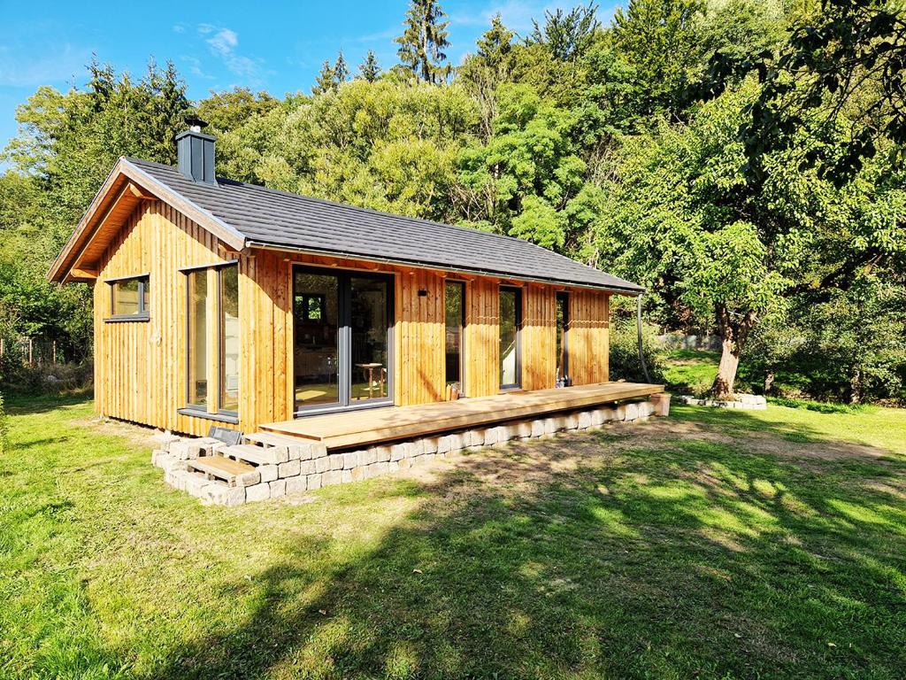 a small wooden cabin with a deck in a field at Holzhaus mit Kamin - Am Forellenfluss 