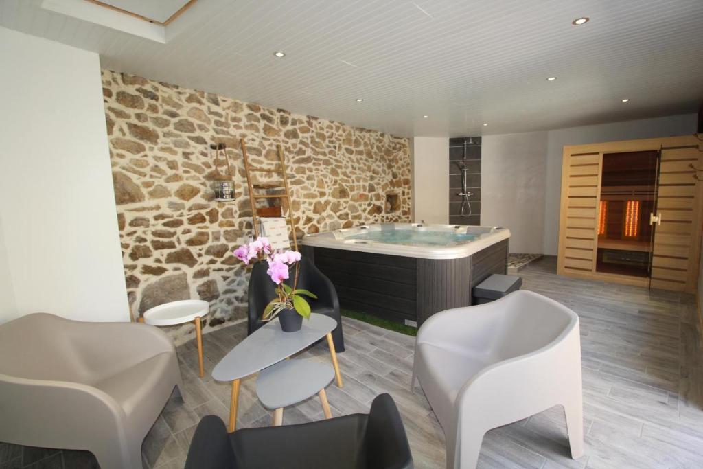 a bathroom with a tub and chairs and a stone wall at La Maison Vieille avec Spa Privé in Savas