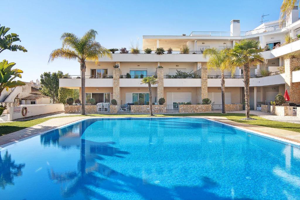 una piscina frente a un edificio con palmeras en Family House White Dove en Olhos de Água