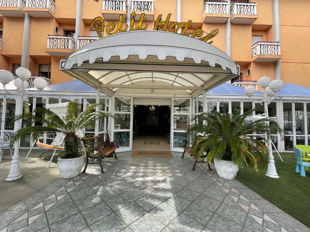 un edificio de hotel con un patio con bancos y palmeras en Petit Hotel, en Caorle