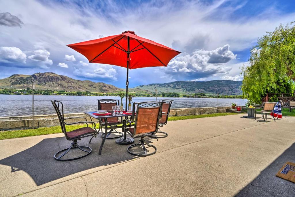 Waterfront Osoyoos Lake Cottage with Beach and Patio! في Oroville: طاولة وكراسي مع مظلة حمراء