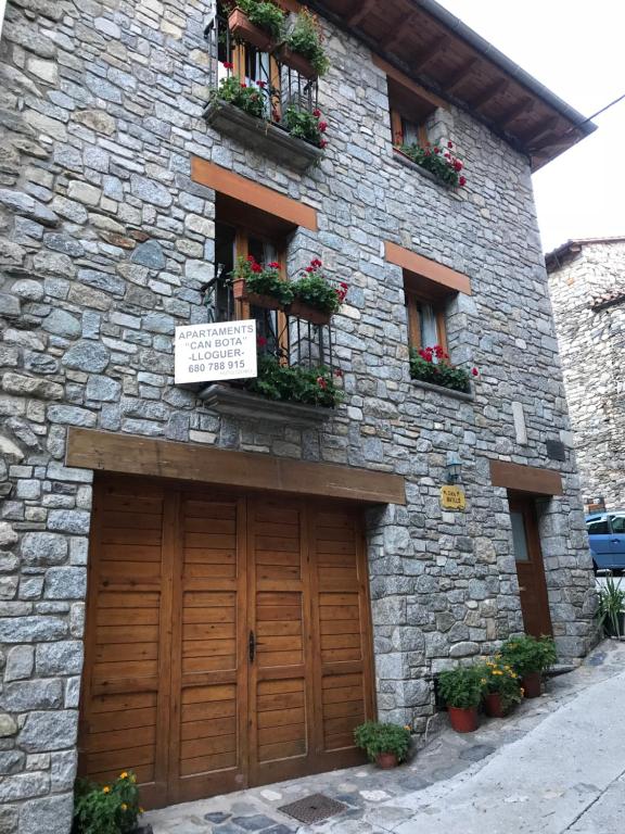 - un bâtiment en pierre avec une porte de garage en bois et des fleurs dans l'établissement Habitatge familiar de Can Bota Batllo, à Setcases