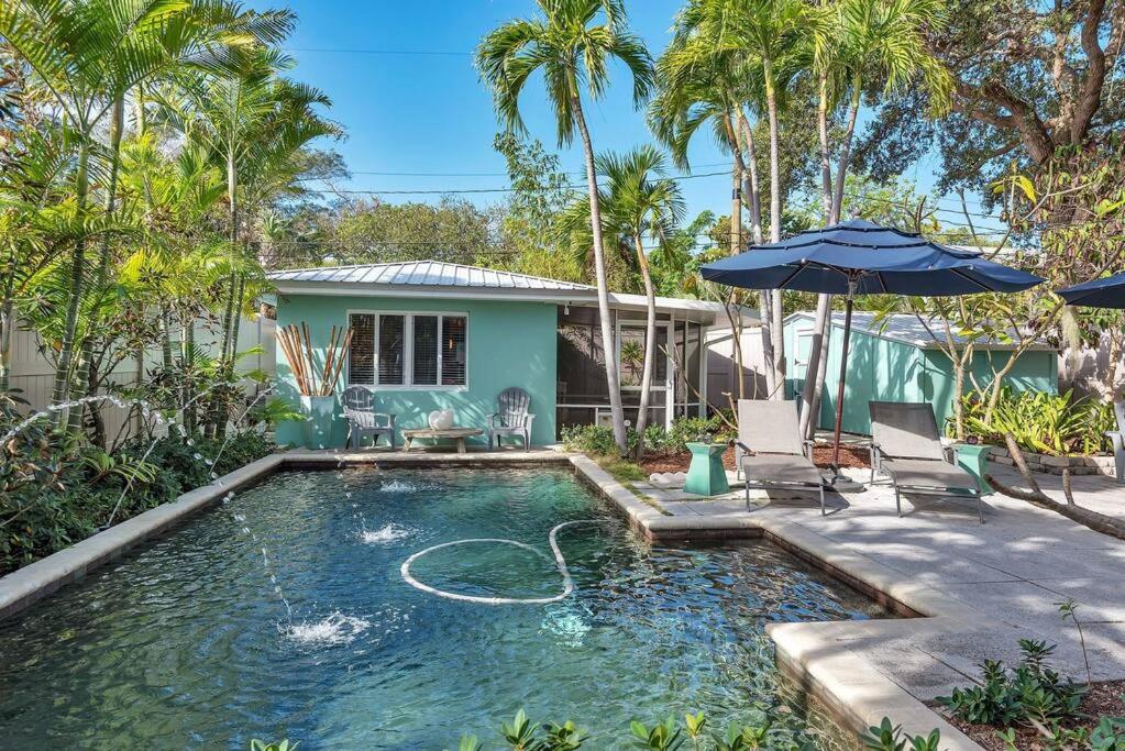 a pool with an umbrella and chairs and a house at Charming Studio w Pool One Mile to Beach Pets Welcome in Lake Worth