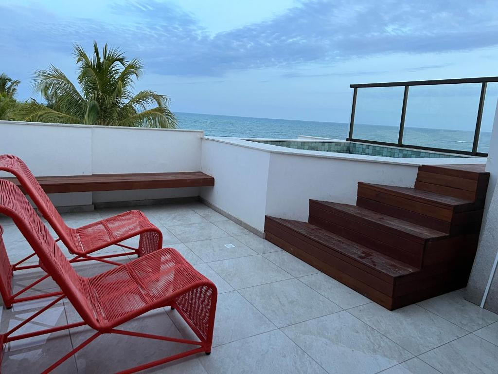 two red chairs sitting on a balcony overlooking the ocean at Casa Califórnia in Itacimirim