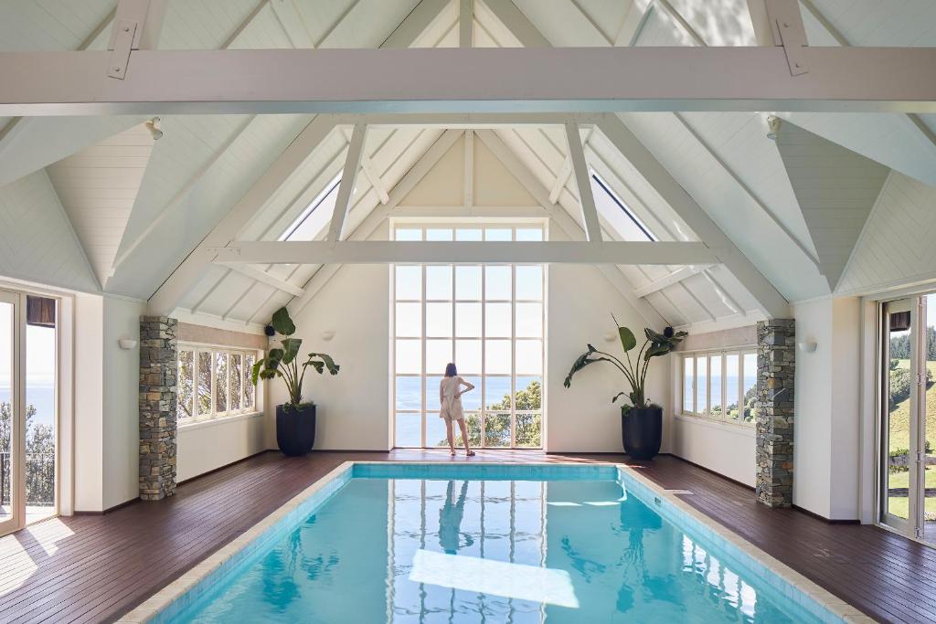 a swimming pool in a room with windows and a person standing in the windowledged at Hillbrook Estate Whangamata in Opoutere