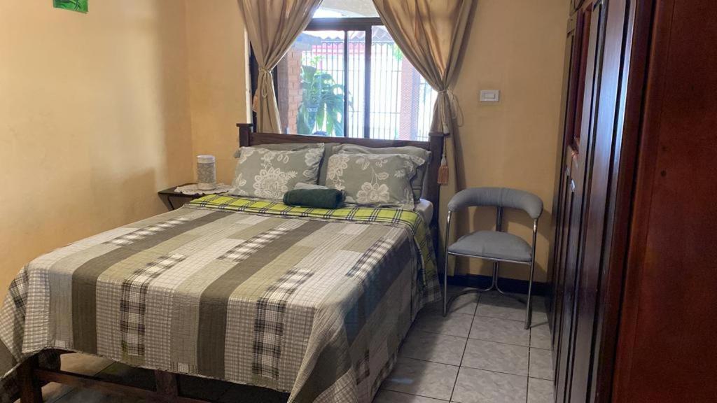 1 dormitorio con 1 cama con silla y ventana en Casa Lupita Alajuela, en Alajuela