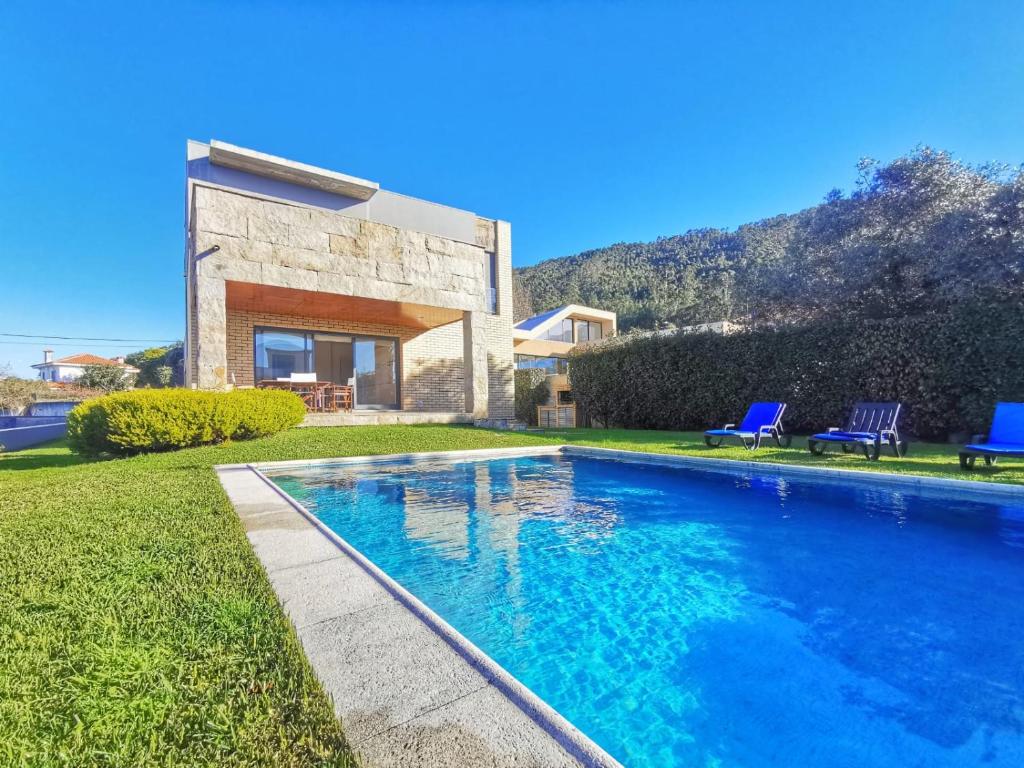 a swimming pool in front of a house with two blue chairs at Hill & Beach house in Viana do Castelo