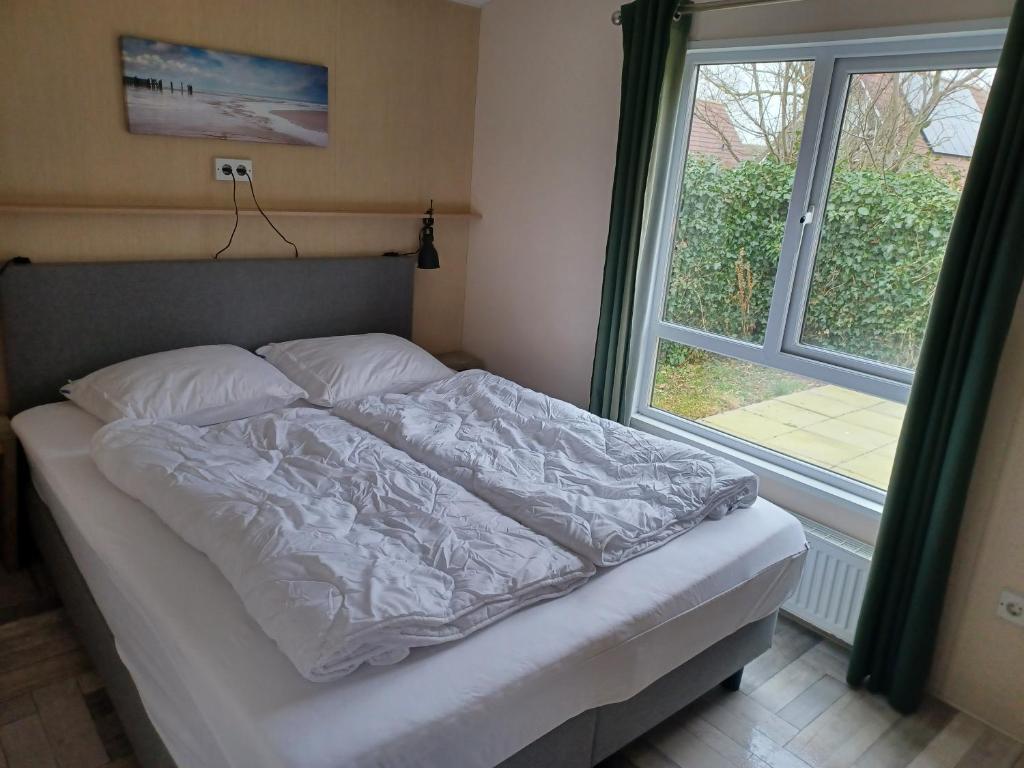 a bed in a bedroom next to a window at Chalet duunzicht Texel in De Cocksdorp