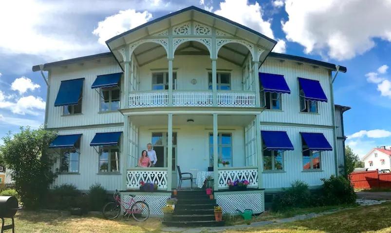 uma mulher de pé na varanda da frente de uma casa azul em Wallinshuset em Sunne