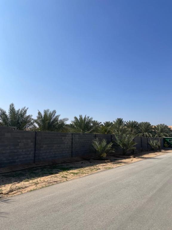an empty road next to a wall with palm trees at مزرعة السلطانية in Buraydah