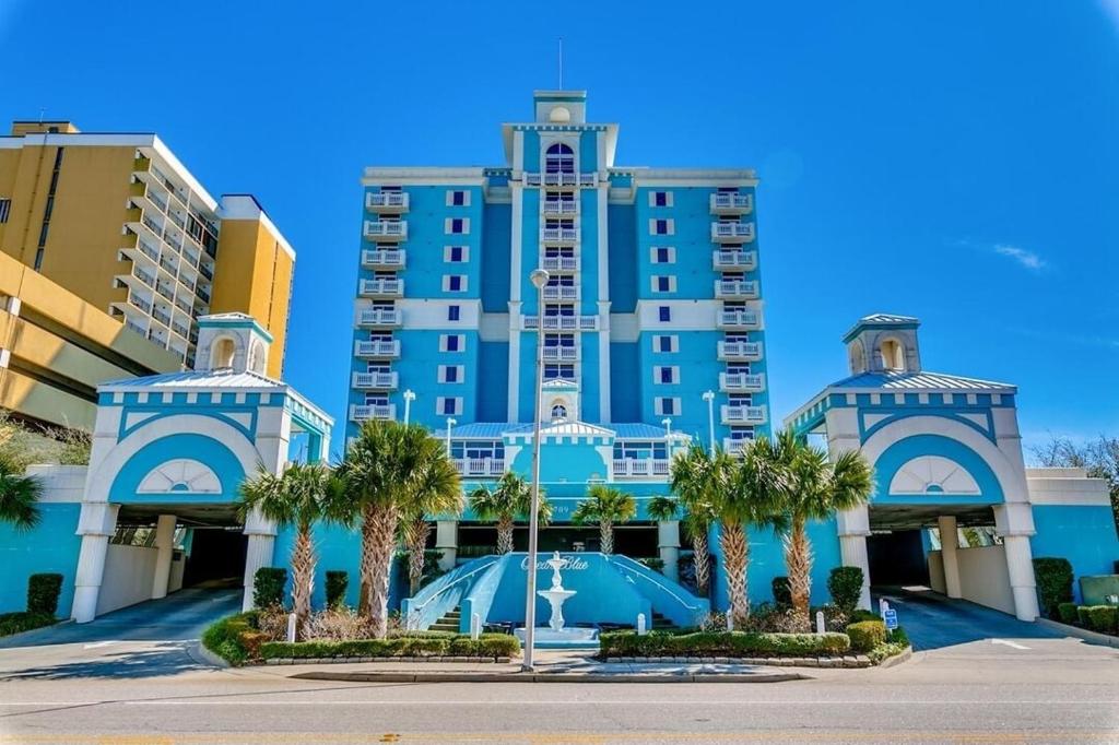 a large blue building with palm trees in front of it at Ocean Blue - Ocean View Condos by Coastline Resorts in Myrtle Beach