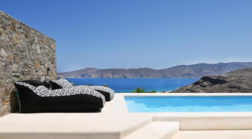uma vista para uma piscina com um sofá e para o oceano em Sea Breeze Mykonos em Panormos Mykonos