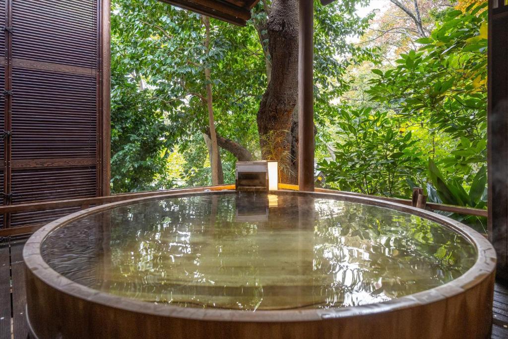 una bañera de hidromasaje en una terraza con árboles al fondo en Jinya Ryokan, en Hadano