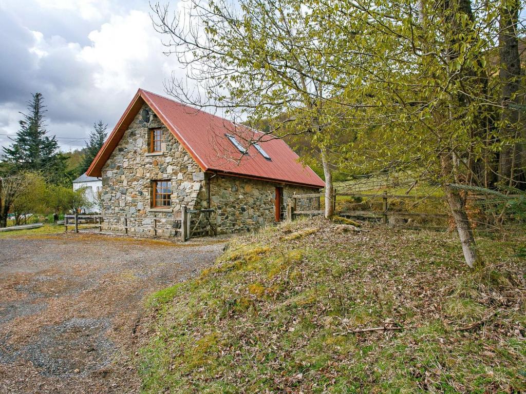 una casa de piedra con techo rojo en un campo en The Barn - S4593, en Lochearnhead