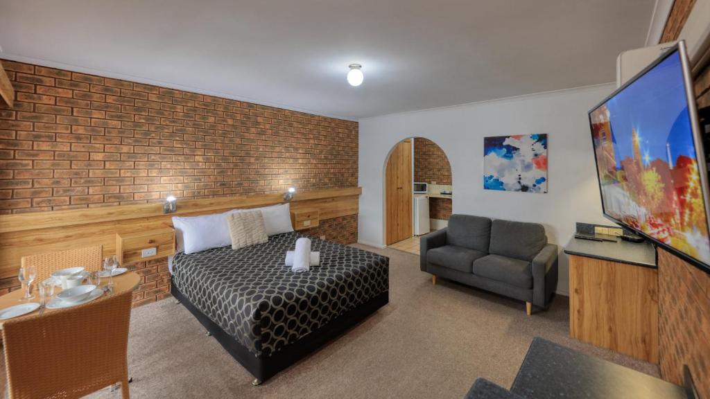 a bedroom with a bed and a chair and a television at The Cottage Motor Inn Albury CBD in Albury