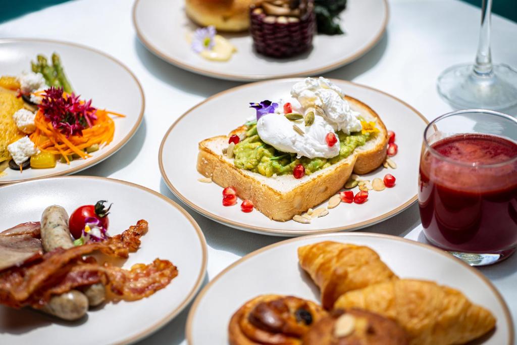 A close-up breakfast table showing avocado toast, bacon and sausages, pastries and red juice.