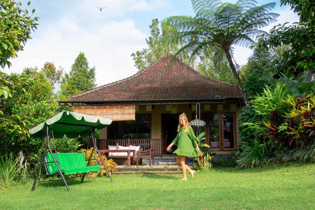 a woman in a green dress walking in front of a house at Amartya Puri Green Cottages in Munduk