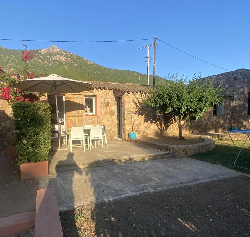 une terrasse avec un parasol, des chaises et une maison dans l'établissement Maison Le Prunier avec piscine - Domaine E Case Di Cuttoli, à Cuttoli-Corticchiato