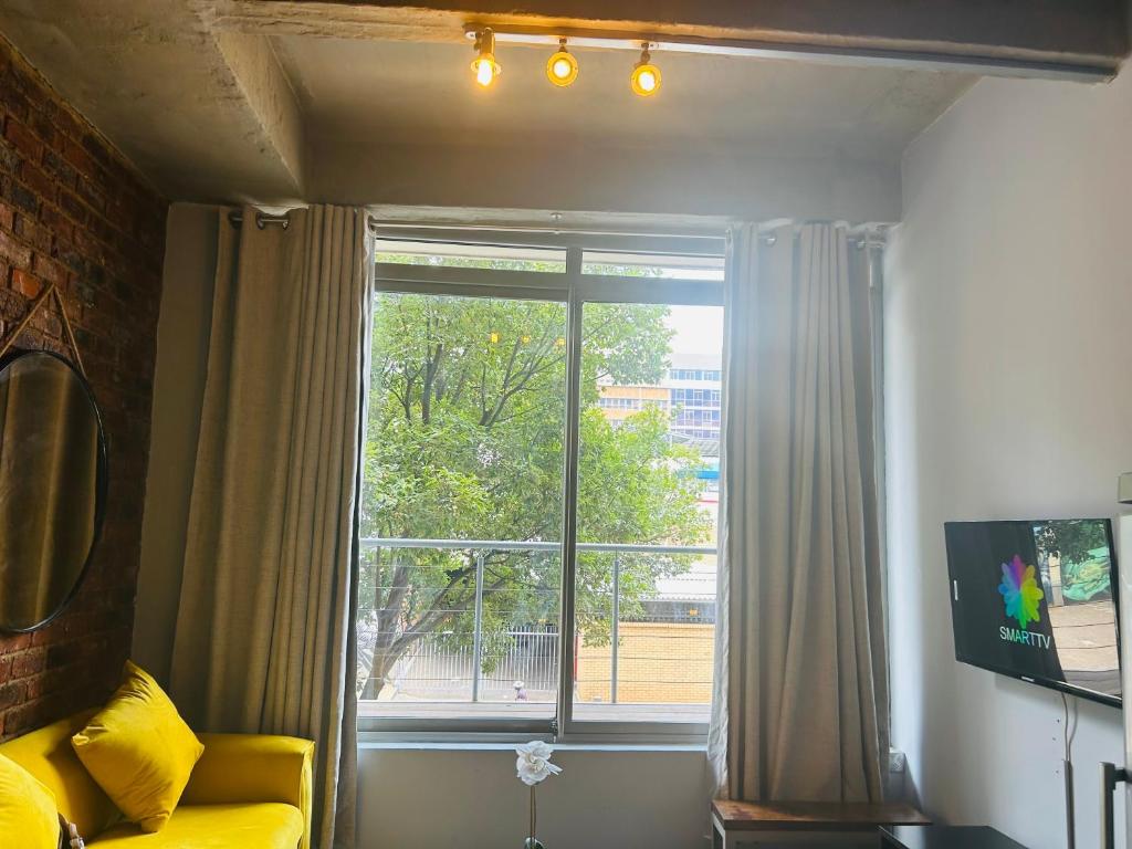 a living room with a large window and a yellow couch at Joburg’s Cutest Condo. in Johannesburg