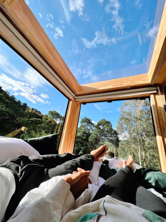 a person laying on a bed looking out a window at LUTS Chalés in Gonçalves
