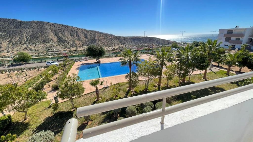 un balcón con vistas a la piscina y a las palmeras. en Appartement vue sur piscine et sur mer en Taghazout