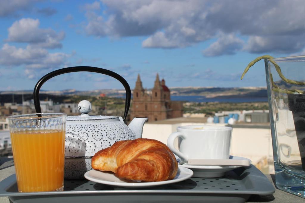 a tray with a croissant and a tea pot and orange juice at Victoria by Petit Chic in Mellieħa