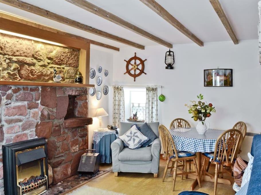 Fisherman's Cottage in Pennan في Pennan: غرفة معيشة مع موقد حجري وطاولة وكراسي