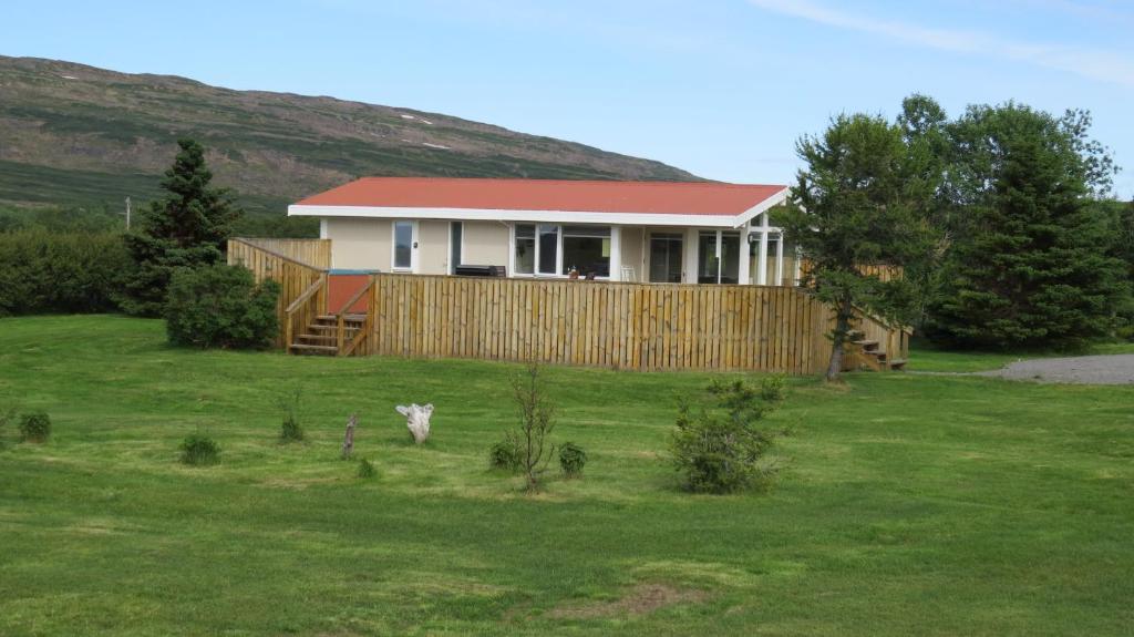 a house with a red roof on a green field at Hvammur 1 with private hot tub in Drangsnes