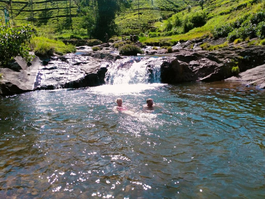 zwei Personen schwimmen in einem Fluss vor einem Wasserfall in der Unterkunft Rock View Rest Hatton in Hatton