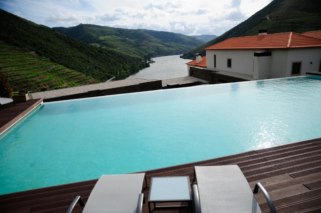 a large swimming pool with chairs and a river at Hotel Rural Quinta Do Pego in Tabuaço