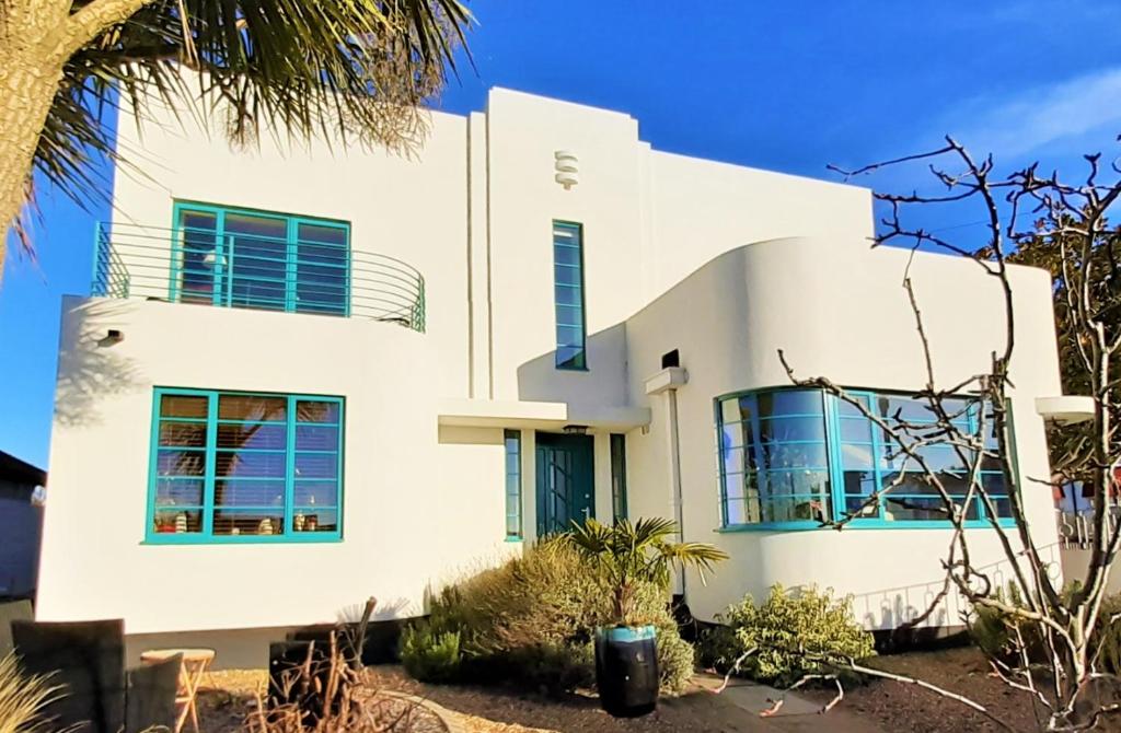 a white house with blue windows and a palm tree at Twentieth Century B&B in Birchington