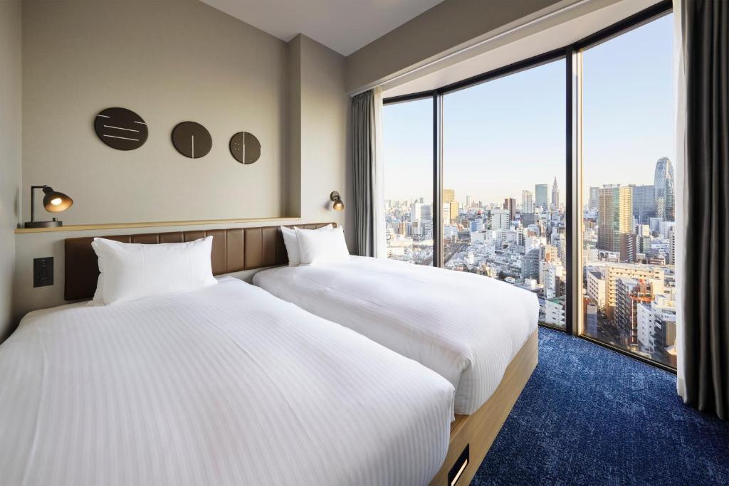 two beds in a hotel room with a large window at Hundred Stay Tokyo Shinjuku in Tokyo