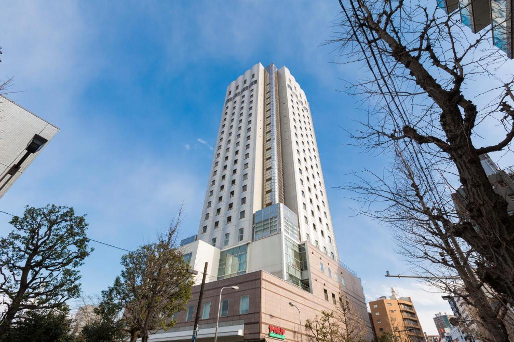 a tall white building with trees in front of it at Hundred Stay Tokyo Shinjuku in Tokyo