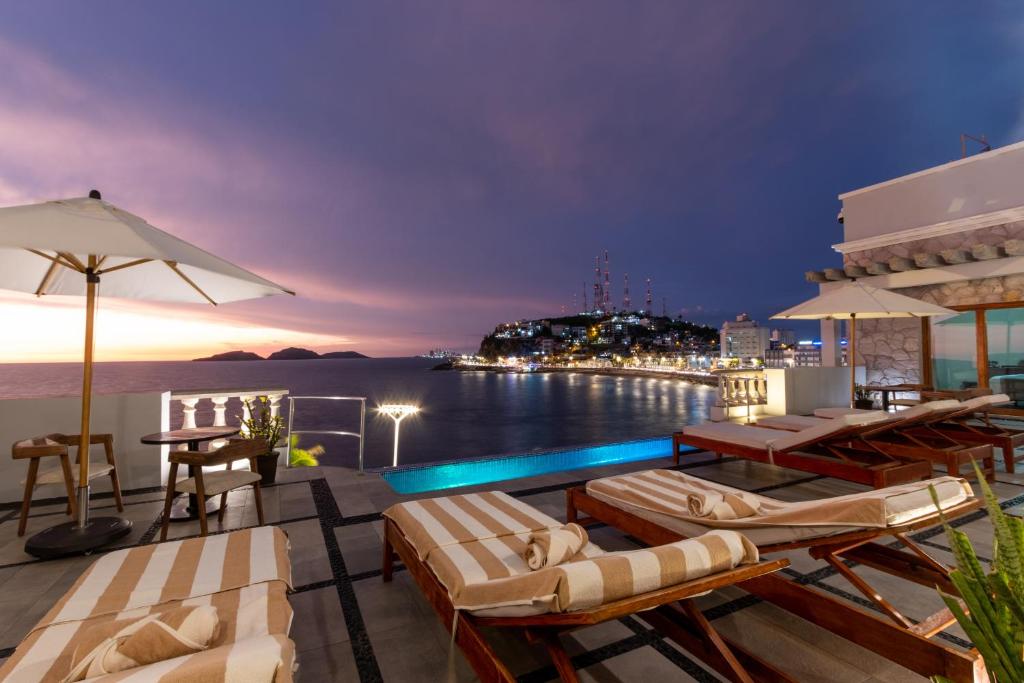 una terraza en la azotea con sillas y una piscina por la noche en Casa Lucila Hotel Boutique en Mazatlán