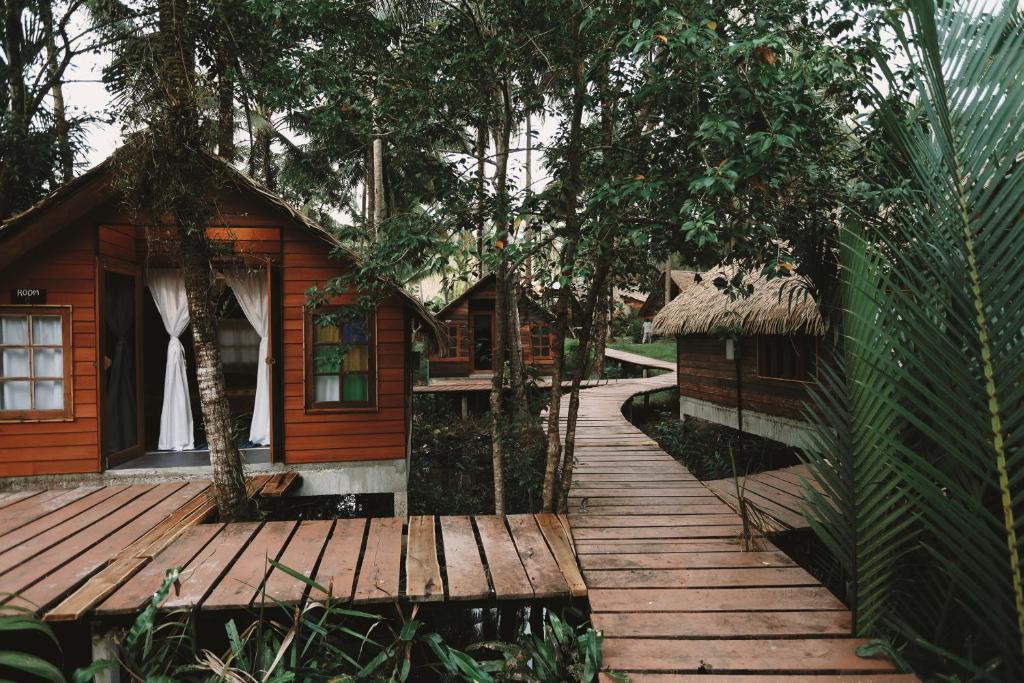a wooden walkway leading to a cabin with trees at Coco Camping Koh Kood in Ban Khlong Chao