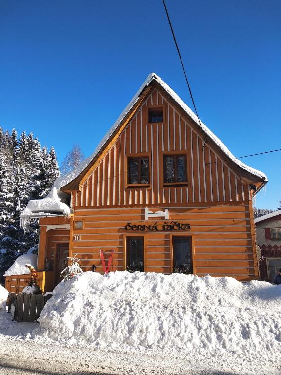 a log cabin with snow in front of it at Apartmány Černá Říčka in Desná