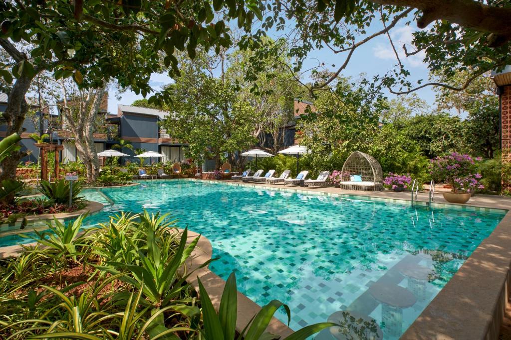 a swimming pool in a resort with chairs and trees at Avataara Resort & Spa in Anjuna