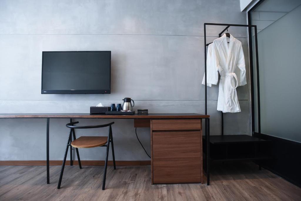 A slim in-room desk runs beneath a wall-mounted television, with a chair and kettle station.