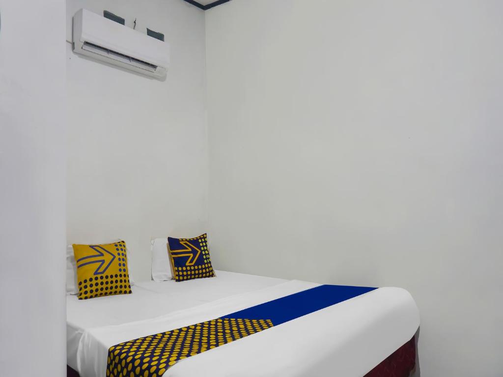 Una cama blanca con almohadas amarillas y azules. en SPOT ON 92154 Nusasari Guest House, en Sukabumi